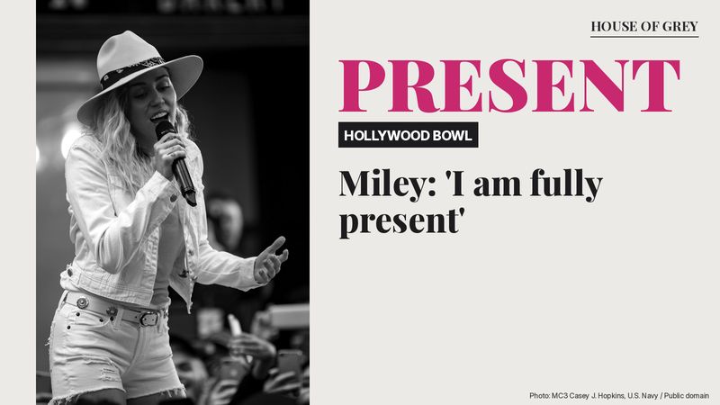 Miley Cyrus in a white hat and white outfit singing into a microphone, with the words 'FULLY PRESENT'