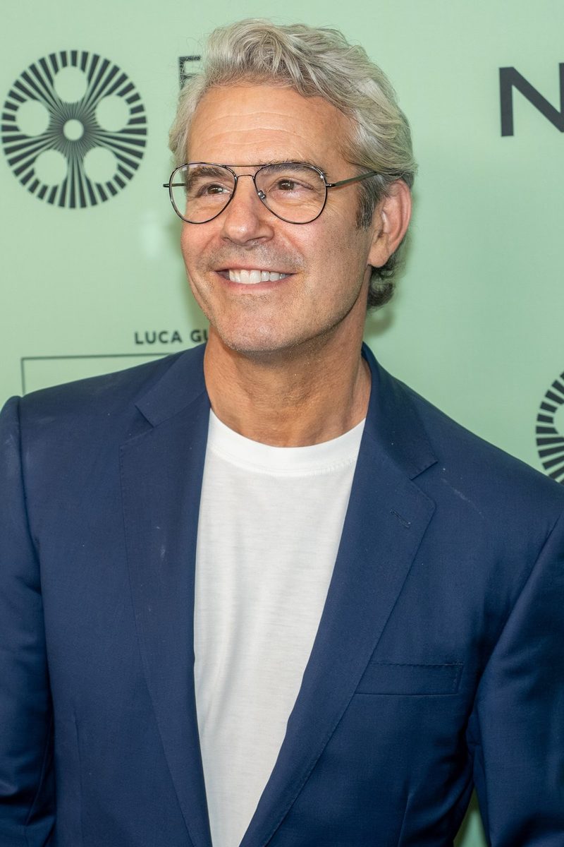 Andy Cohen in glasses, a blue blazer and a white T-shirt in front of a green festival backdrop