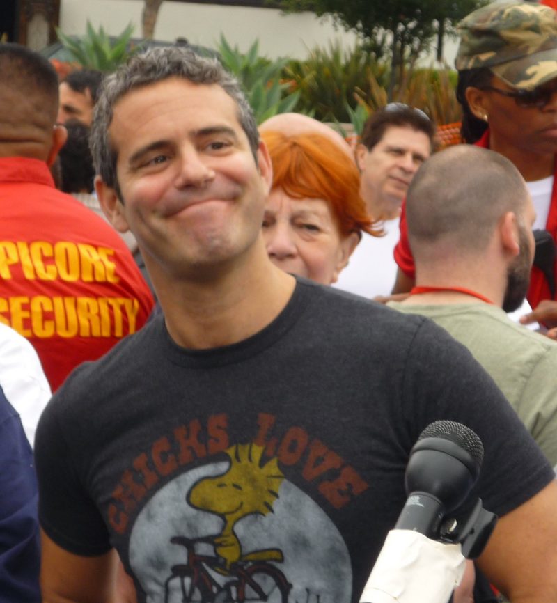 Andy Cohen smiling in a grey graphic T-shirt in a crowd outdoors in 2008