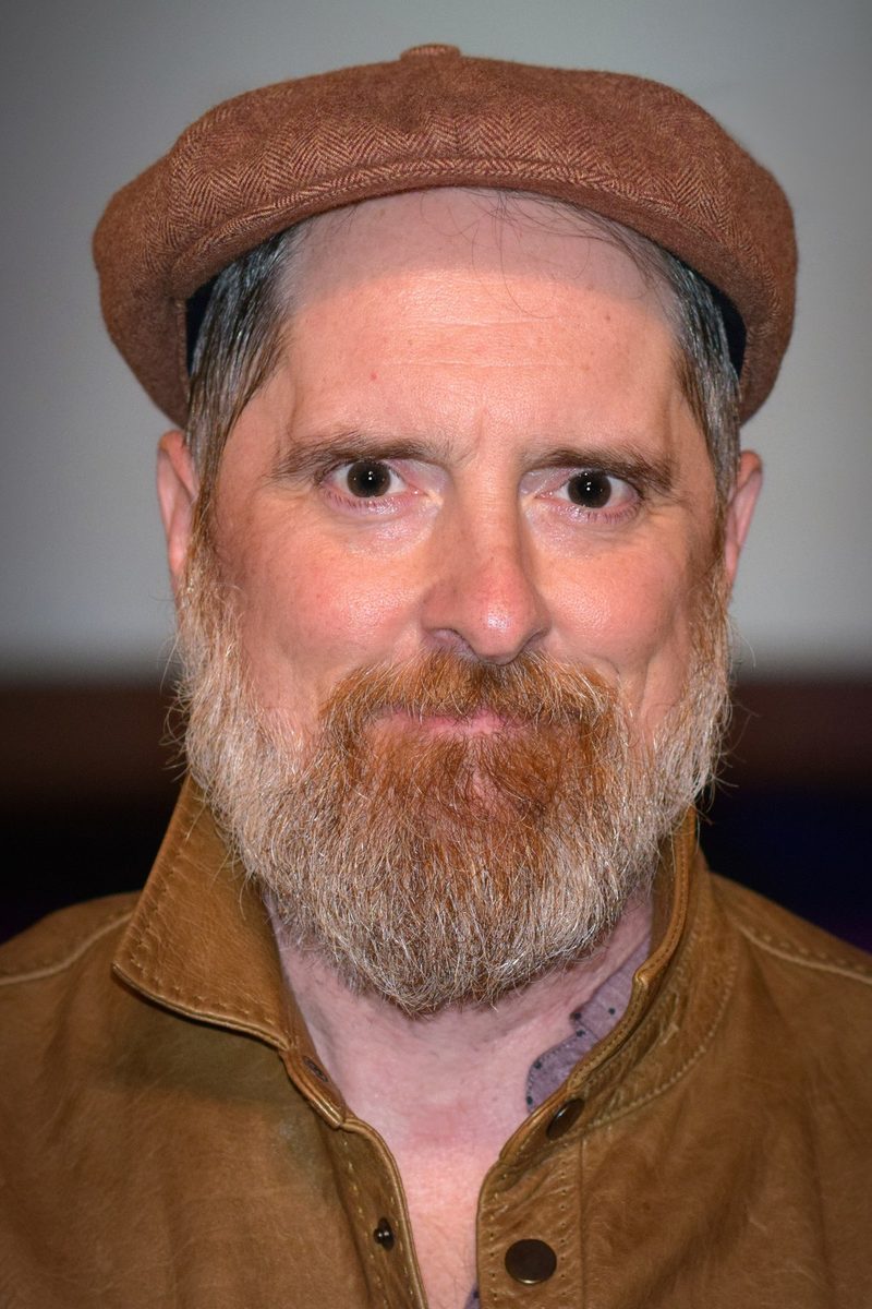 Brendan Hunt with a red beard and a brown flat cap, looking at the camera