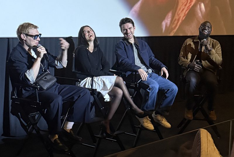 Four people seated on stage chairs at a film Q&A, one speaking into a microphone