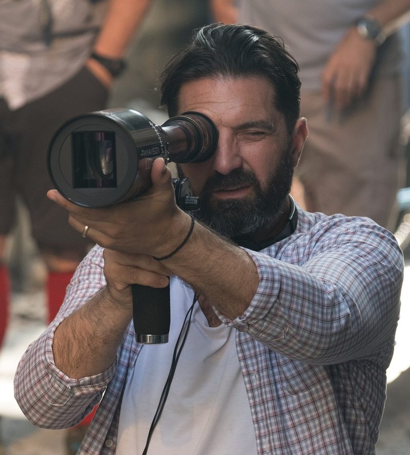 Drew Pearce in a plaid shirt holding a director's viewfinder on a film set