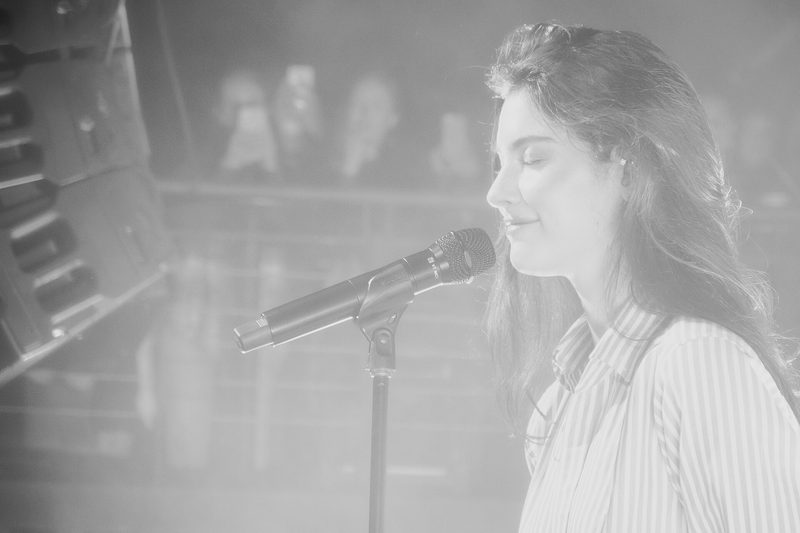Black-and-white photo of Gracie Abrams singing into a microphone on stage
