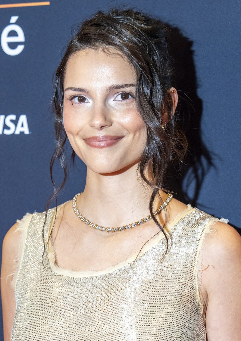 Inde Navarrette with dark wavy hair pulled back, in a gold sleeveless top and a delicate necklace