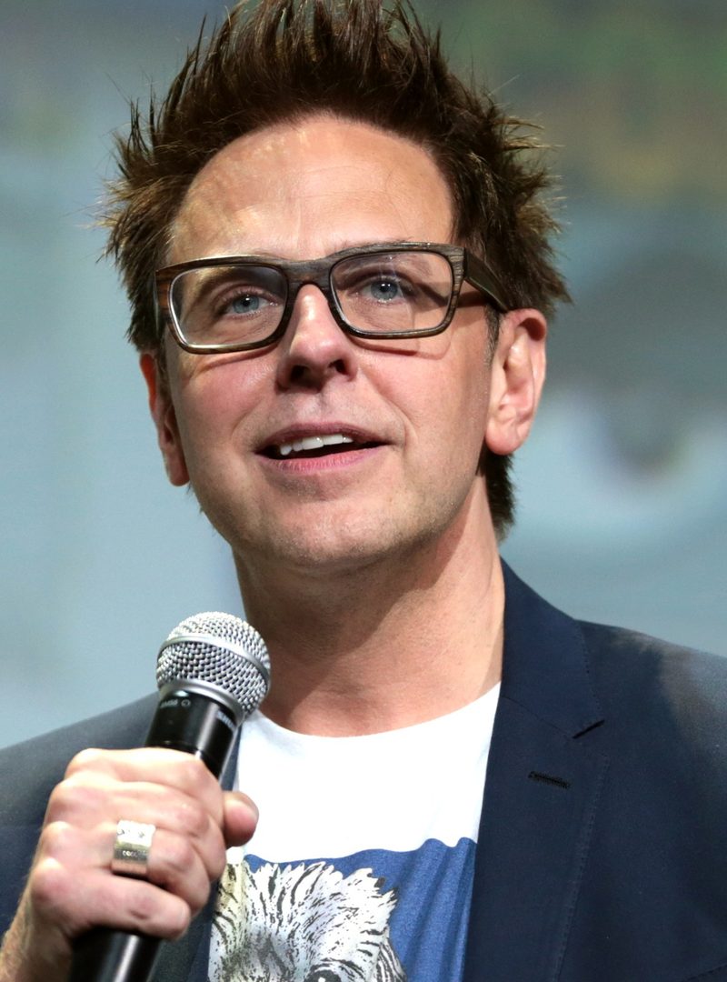 James Gunn in glasses speaking into a microphone