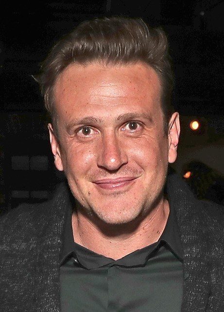 Jason Segel smiling in a dark jacket at night