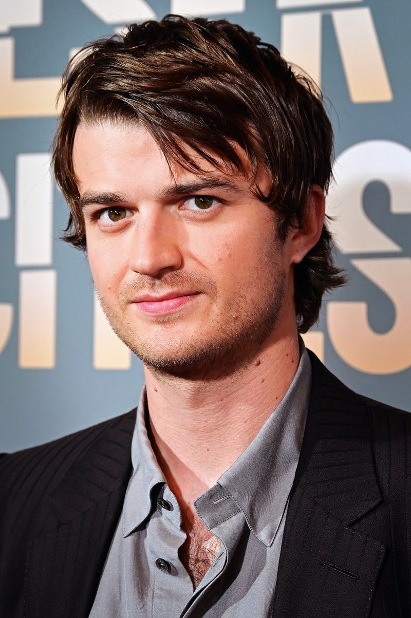 Joe Keery with tousled brown hair in a dark jacket and grey shirt at the opening night