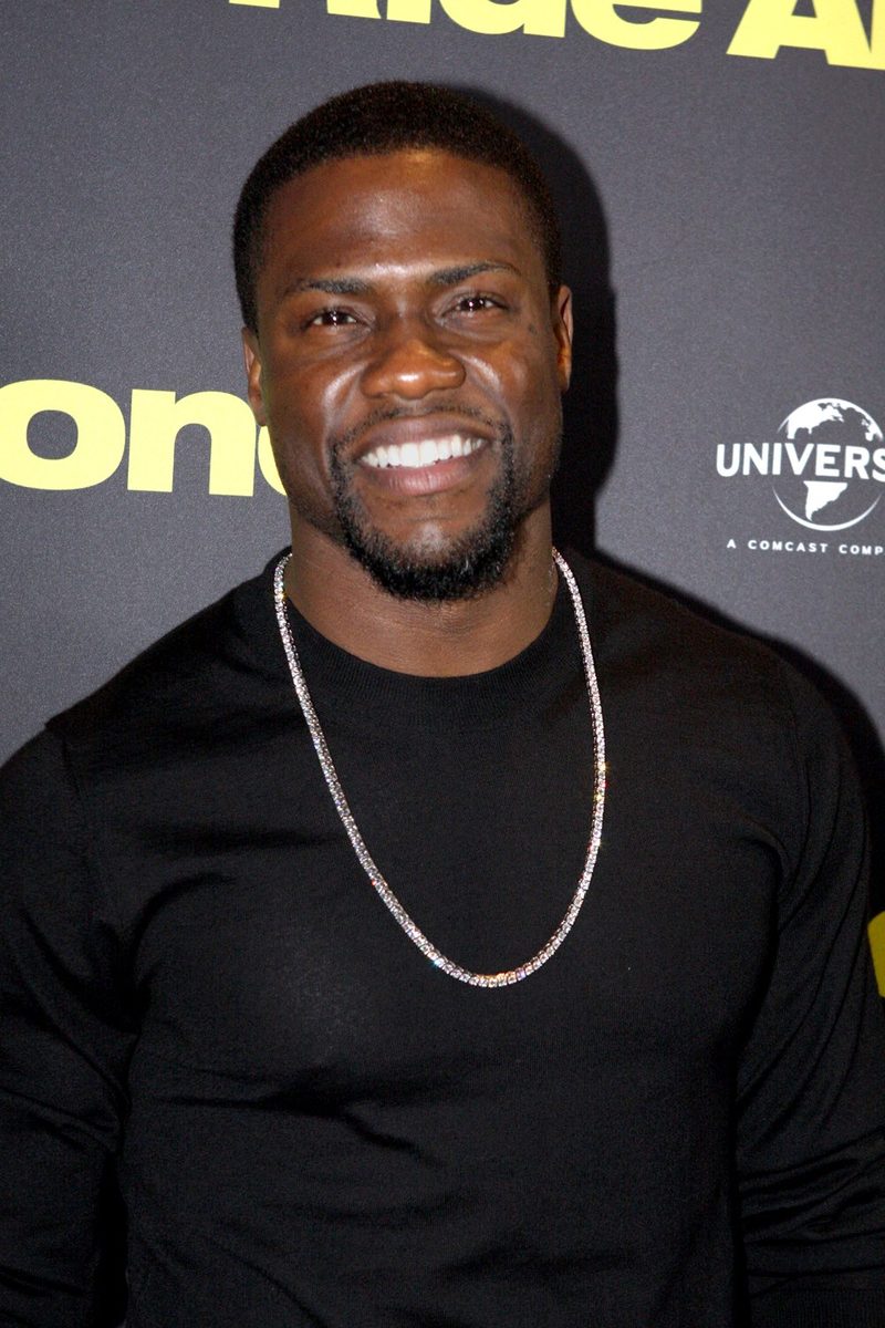 Kevin Hart smiling in a black T-shirt and chain at a premiere