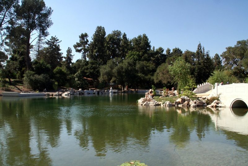 A calm lake surrounded by trees, rocks and a white stone bridge
