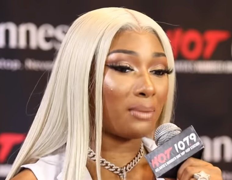 Megan Thee Stallion with long platinum blonde hair speaking into a Hot 107.9 microphone