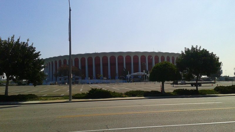 The round, columned exterior of the Forum in Inglewood behind an empty parking lot and trees